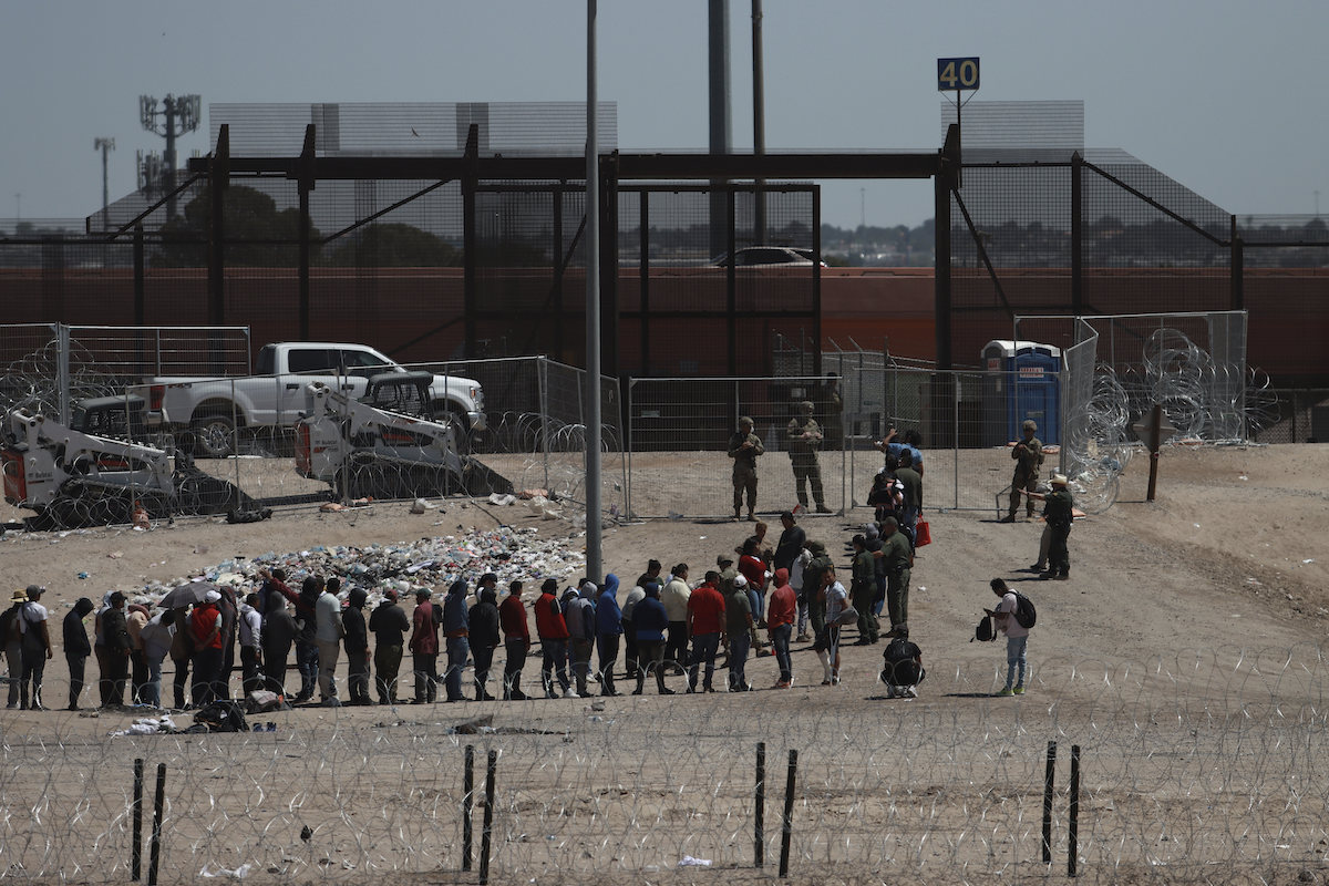 Line of migrants outside border fence with Border Patrol