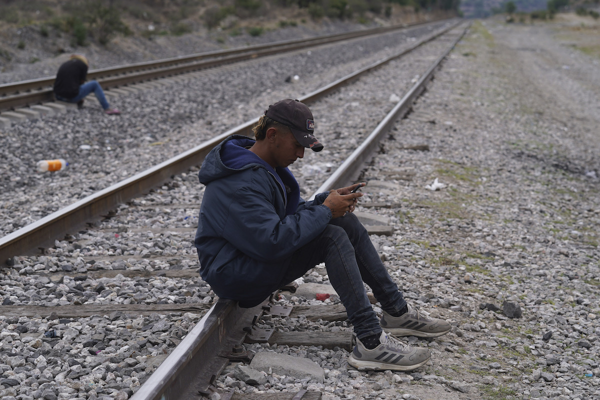 SPANISH: migrant man sitting on tracks on his phone
