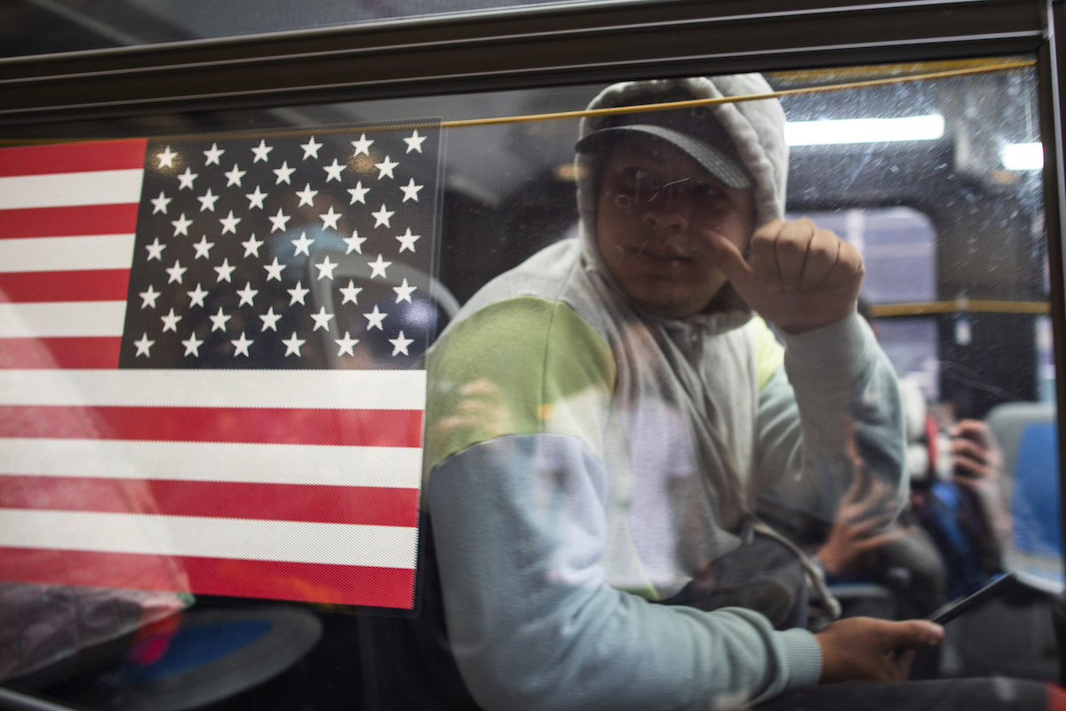 Migrant in a bus arriving in NYC next to a us flag, 5-19-2023