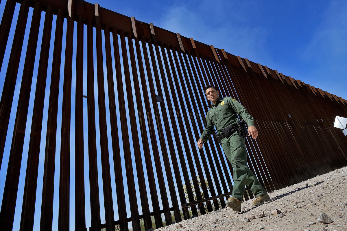Border patrol agent walks alongside border wall in Lukeville, Ariz., 8-29-2023