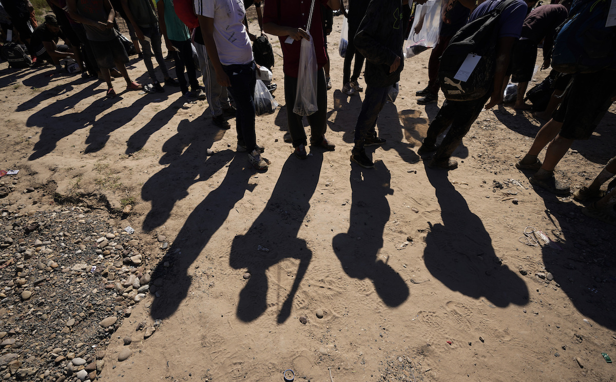 Line of migrants feet at the border with their shadows showing on the ground, Eagle Pass, Texas, 10-19-2023