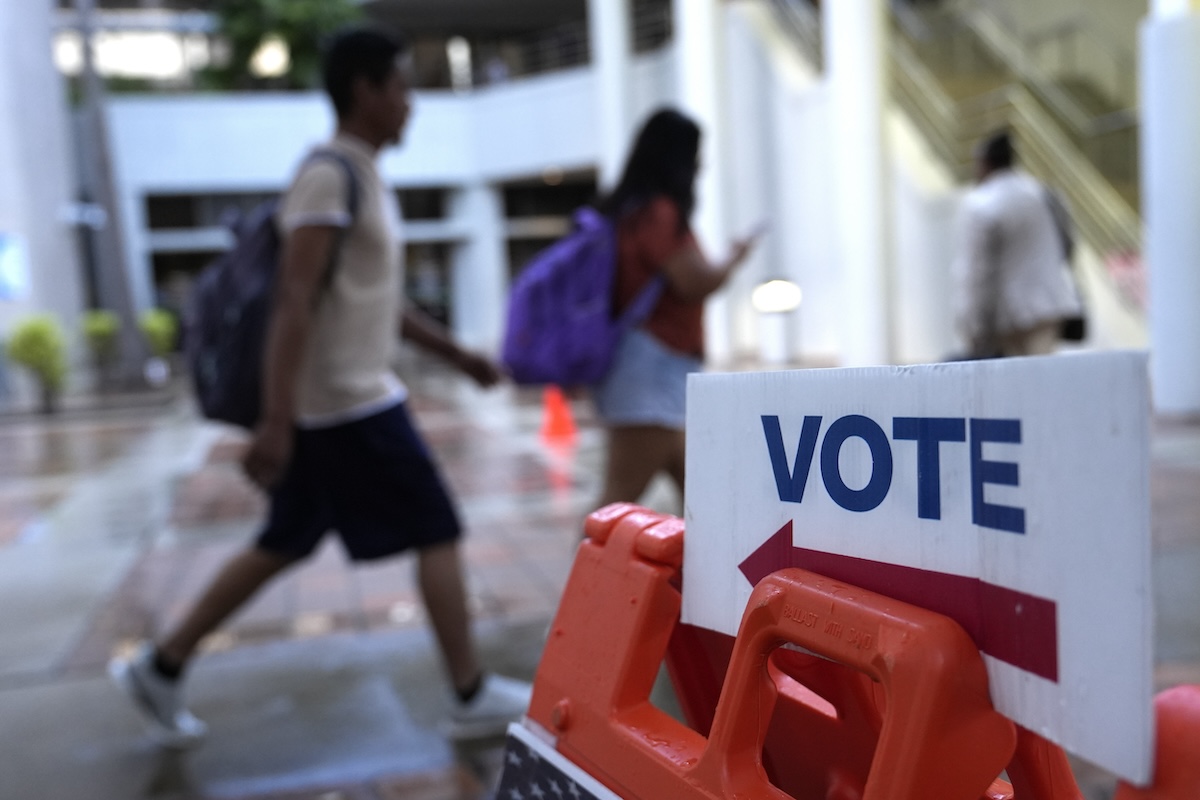 People walk past a sign saying vote - generic