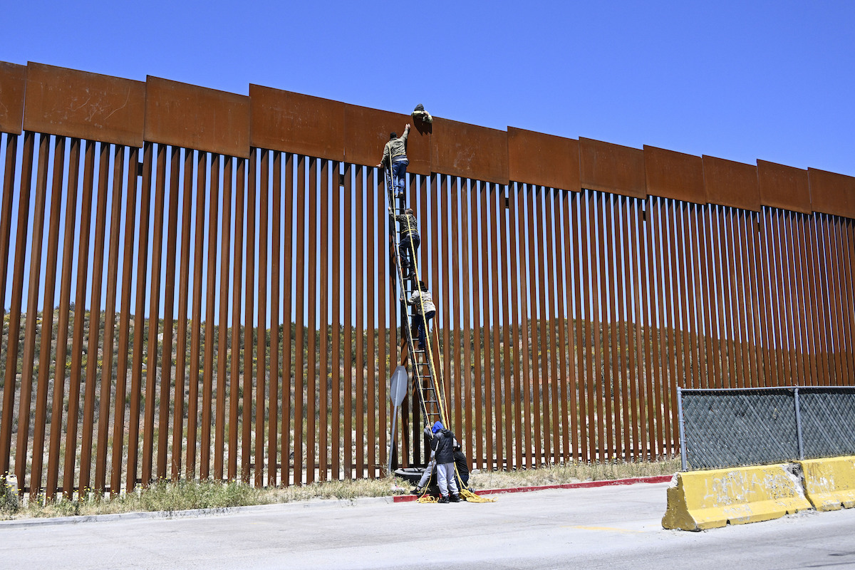 Mexico border wall with ladder and people crossing over it