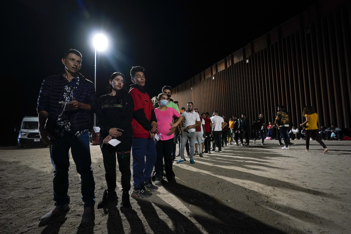 Migrants wait along a border wall on Aug. 23, 2022, after crossing from Mexico