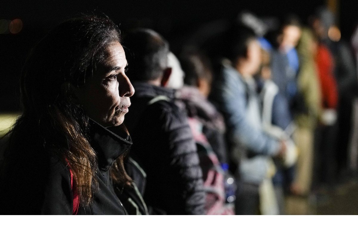 Woman at the border, with line of migrants out of focus behind her. Jan 2023
