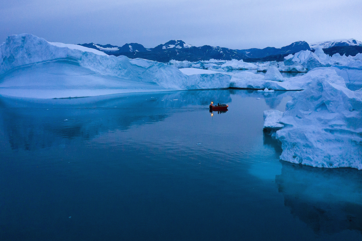 A boat floats between icebergs in Greenland.