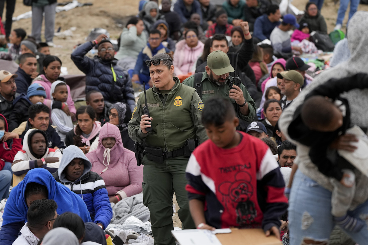 Border patrol agents standing among a crowd of migrants sitting May 12 2023