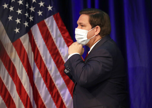 DeSantis with a mask in front of a flag June 2020