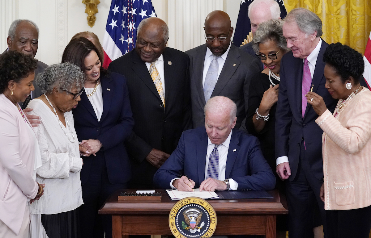 Joe Biden signs Juneteenth in 2021, at desk with people