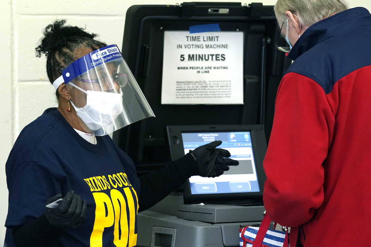 Poll worker in face shield helping voter at machine Mississippi 11-3-20