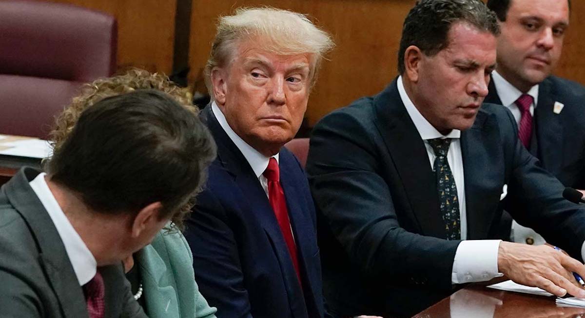 Spanish caption — Trump arraignment sitting with lawyers 4-4-2023
