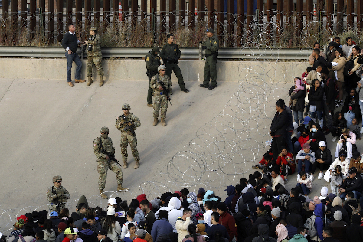 Migrants at border wall with Texas national guard on the side