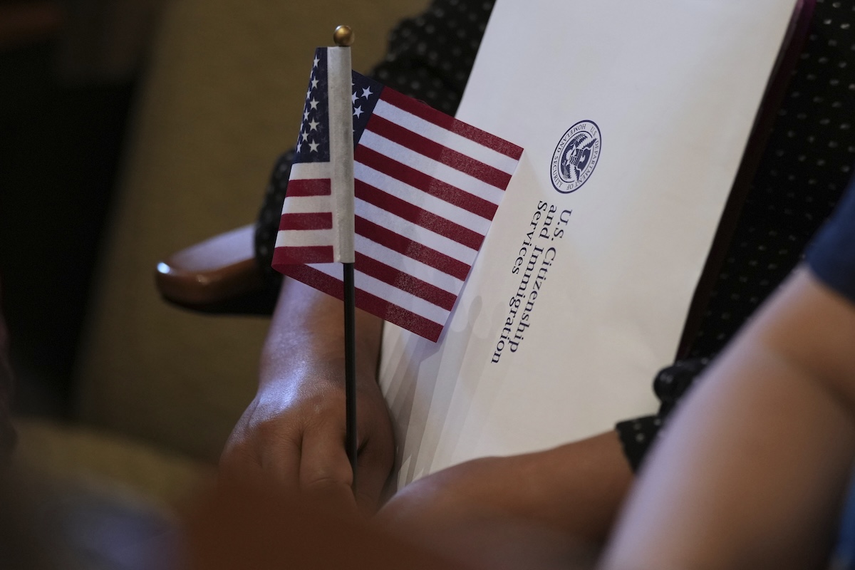 Woman holding flag and USCIS envelope during naturalization ceremony 07-03-25