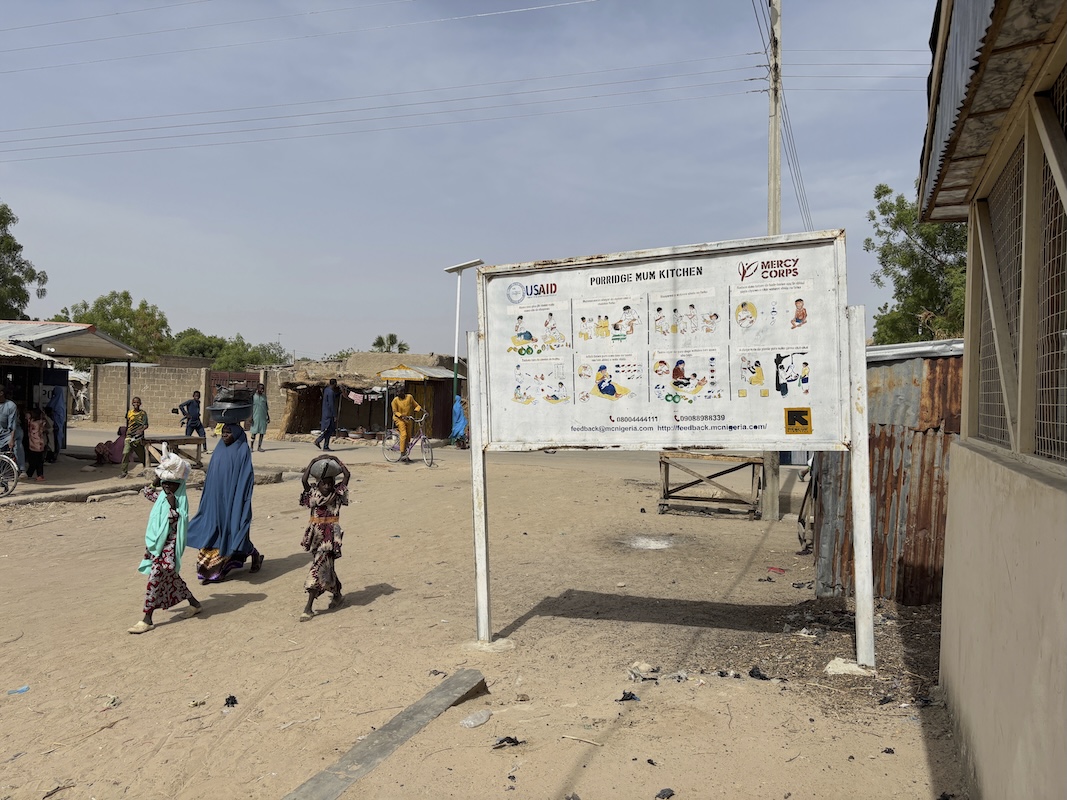 A woman and her children walk past a USAID sign post in Nigeria 04-29-2025