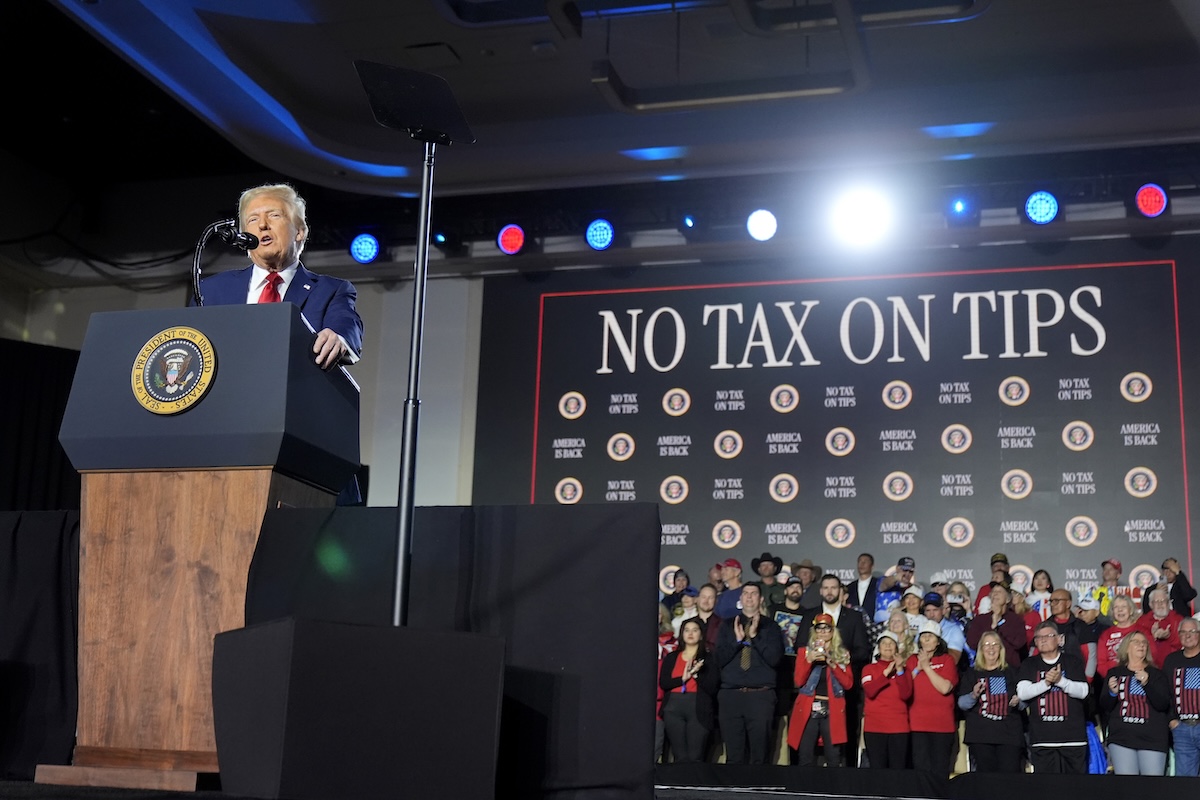 Trump standing in front of No Tax on Tips sign