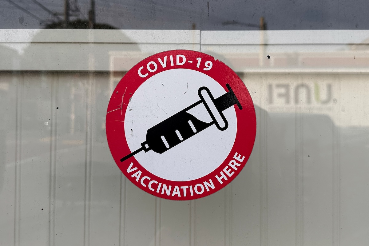 COVID-19 vaccination here sticker on pharmacy window Jan 2026