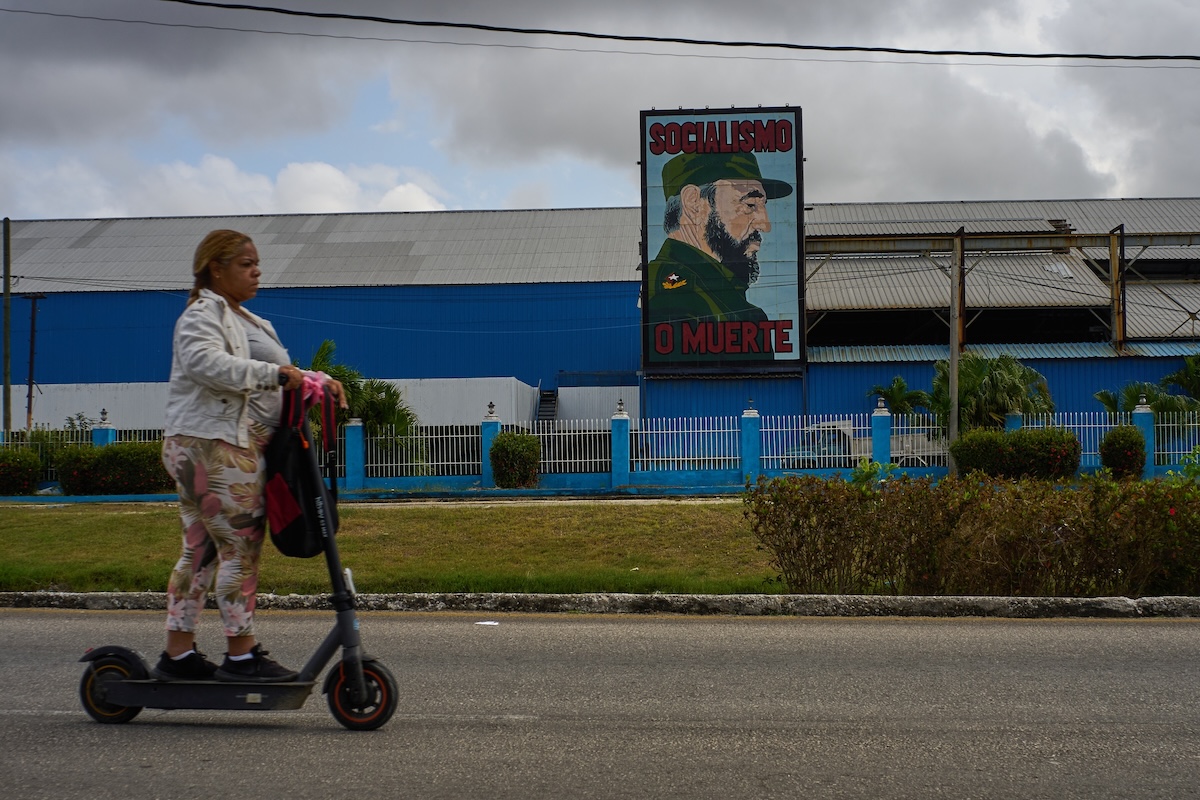 Woman on scooter in front of Castro poster in Cuba March 2026